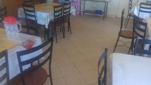 Un comedor con varias mesas y sillas, piso de baldosas y una cocina al fondo.