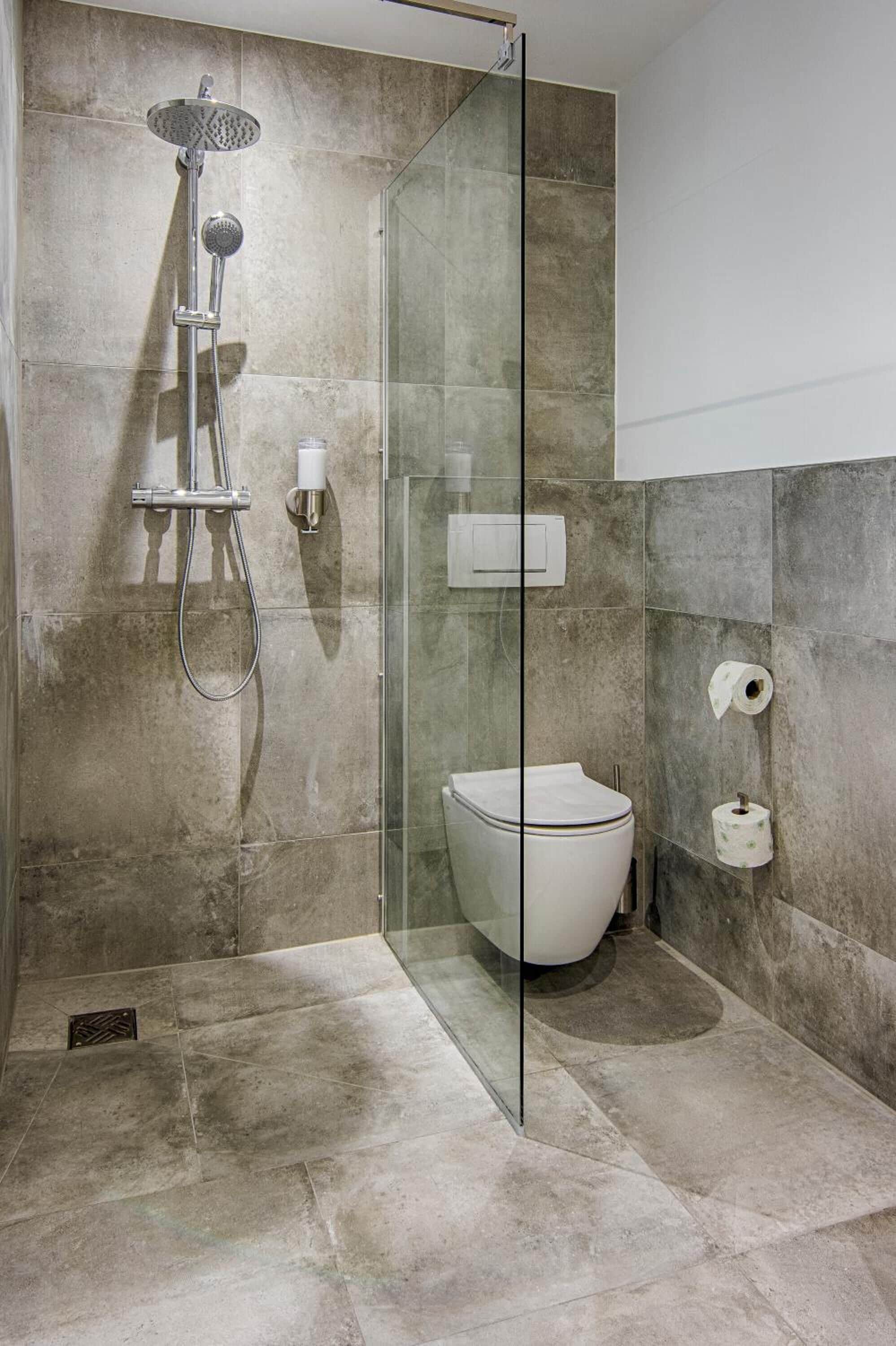 Een moderne badkamer met een douchecabine van glas, een toilet en een papieren handdoekdispenser.