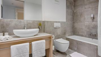 A modern bathroom with a large white sink, a toilet, and a bathtub. There are towels on the counter and a mirror above the sink.