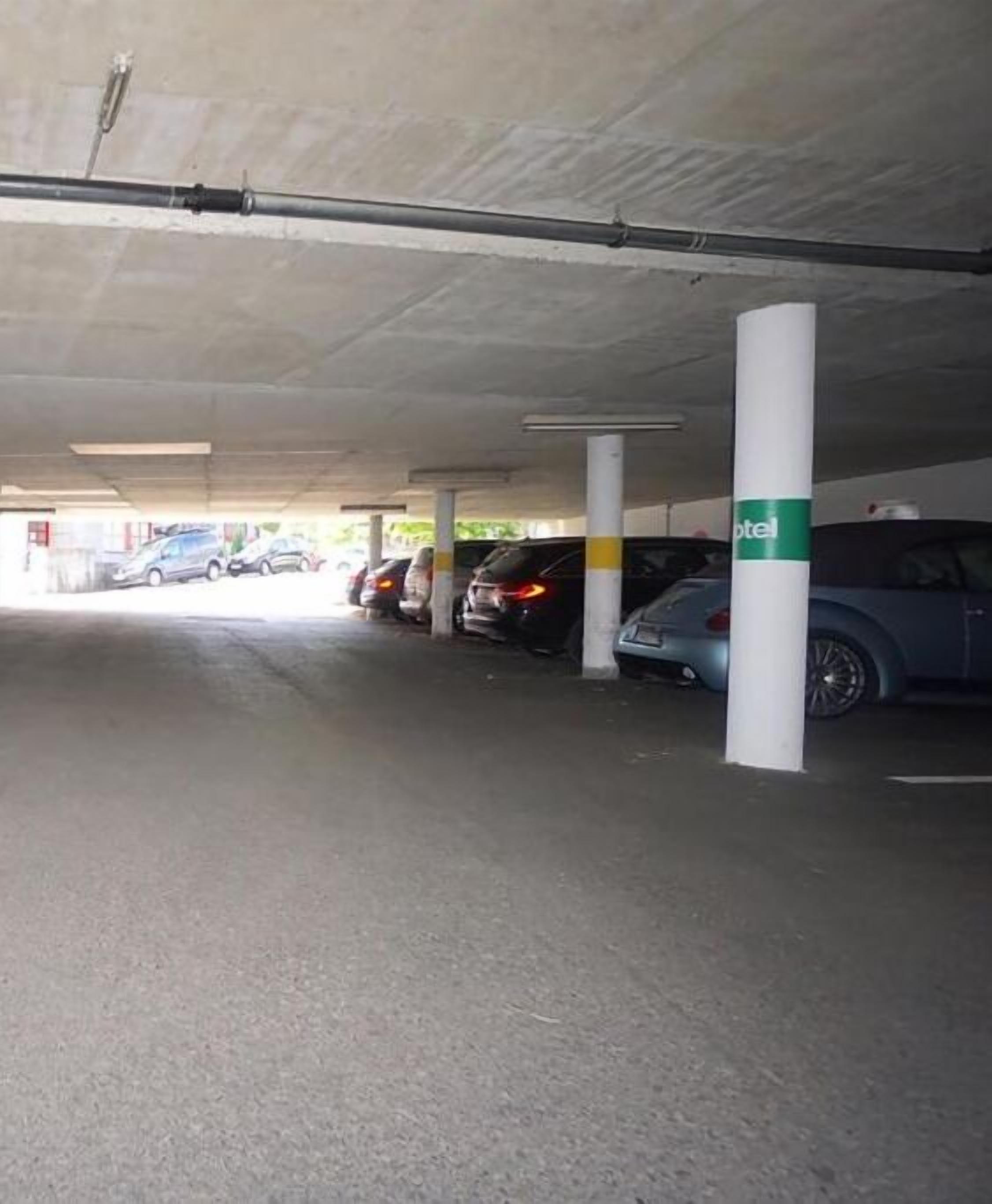 Un estacionamiento subterráneo con varios autos estacionados, pilares de concreto y un letrero que dice "hotel" visible en uno de los pilares.