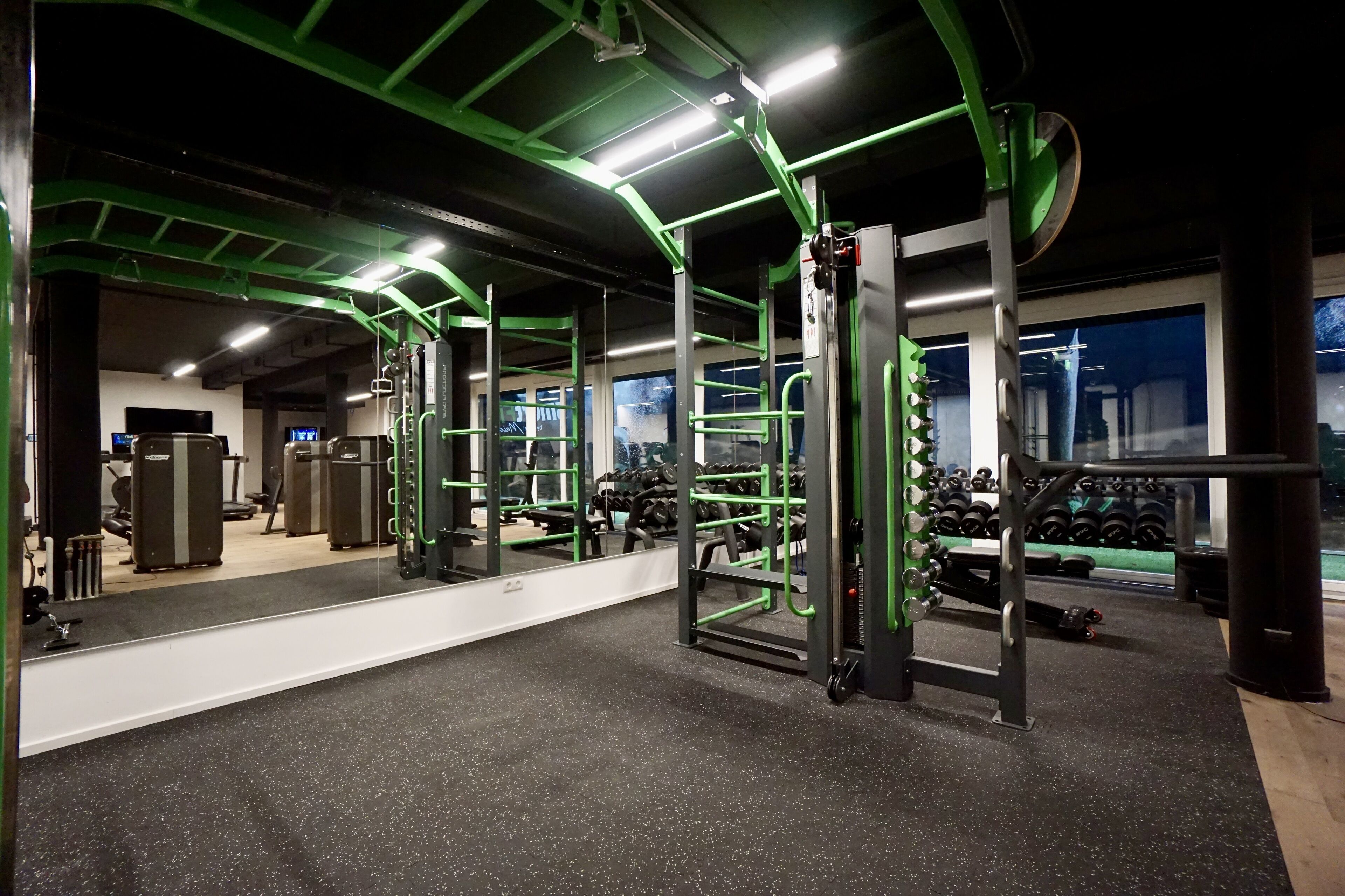 A gym with green equipment, a large mirror, and weight racks.