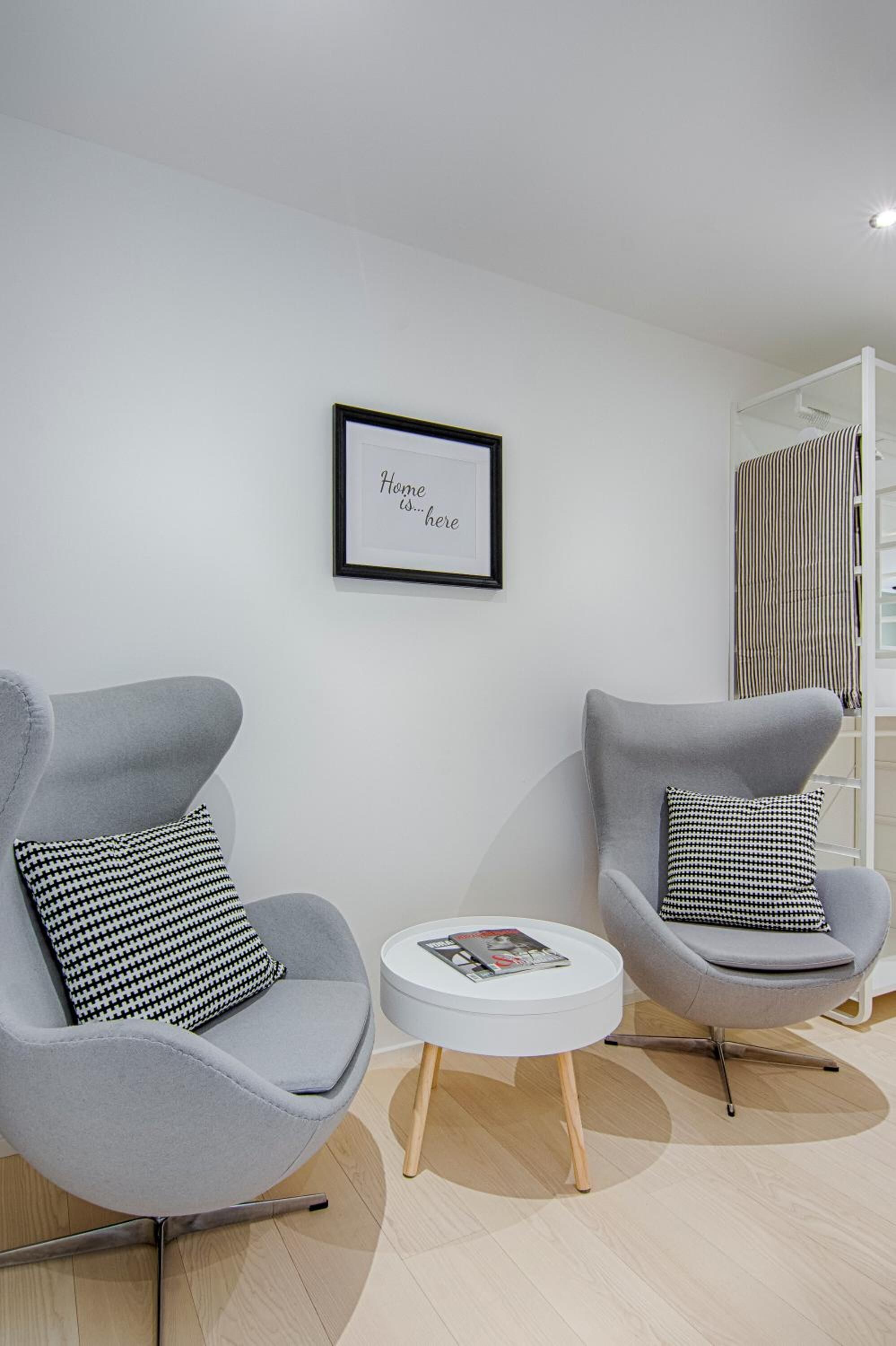 A modern living room with two grey armchairs, a white side table, and a framed quote on the wall.