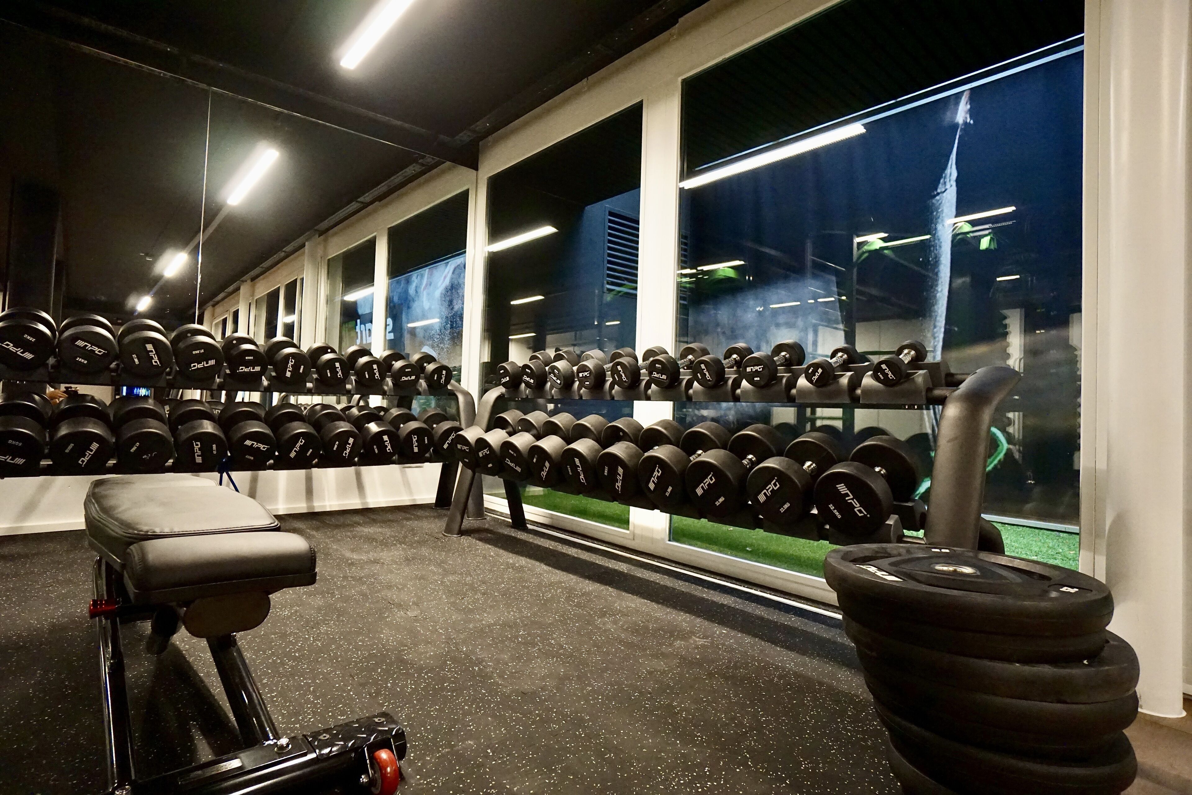 A gym with rows of dumbbells, a bench, and a treadmill.