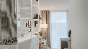 A modern, well-lit room with a built-in wardrobe, a desk with a chair, a lamp, and a window with curtains.