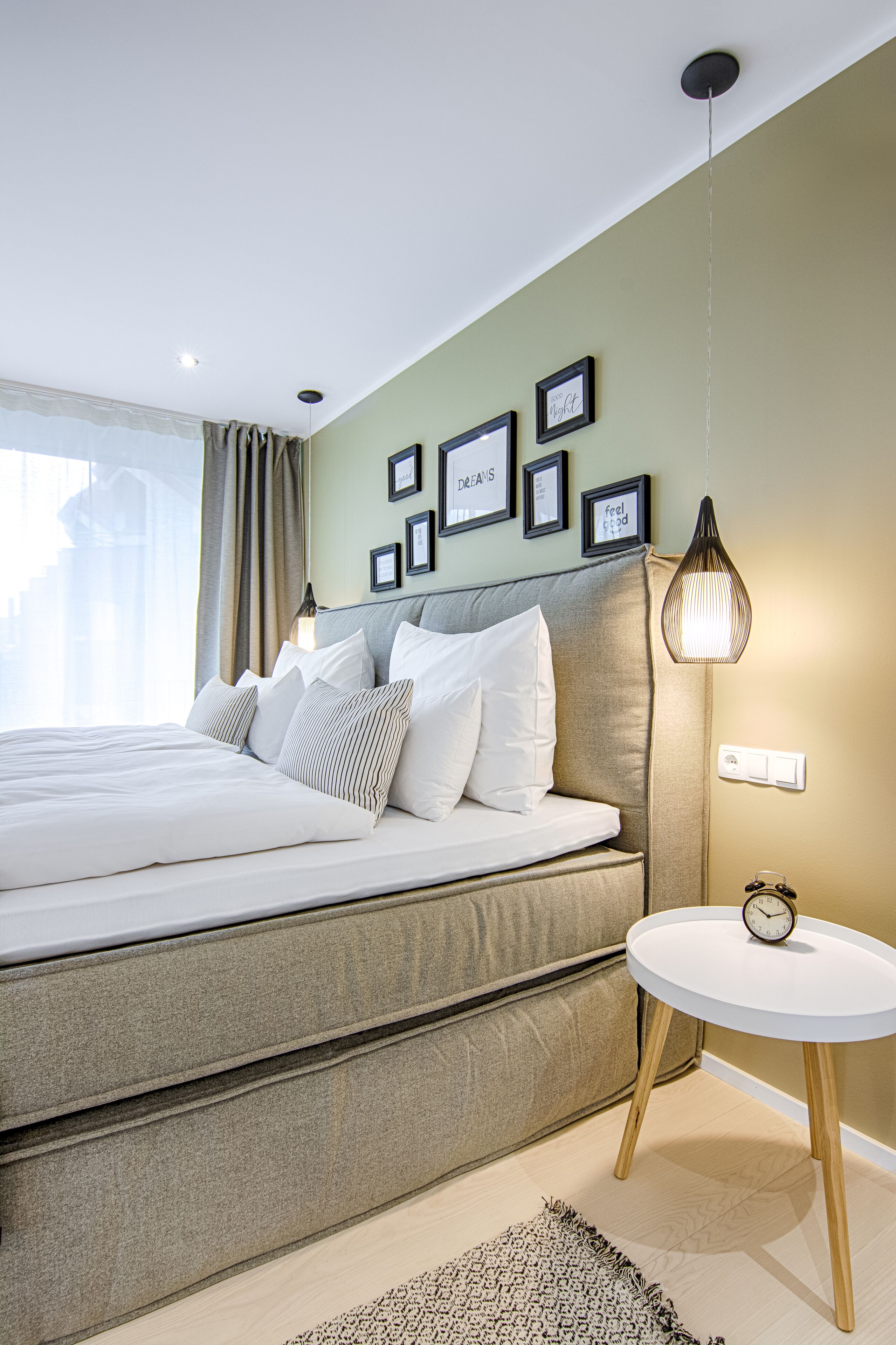 A modern bedroom with a large bed, a bedside table with a clock, and framed pictures on the wall.