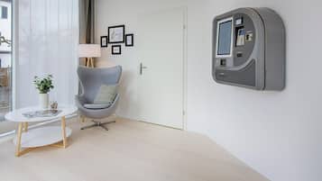 Una habitación moderna con un sillón gris, una mesita blanca pequeña, una lámpara y un televisor montado.