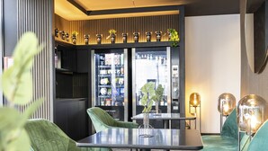A modern interior with a dining area featuring a table and chairs, a kitchen area with a refrigerator, and a vending machine.