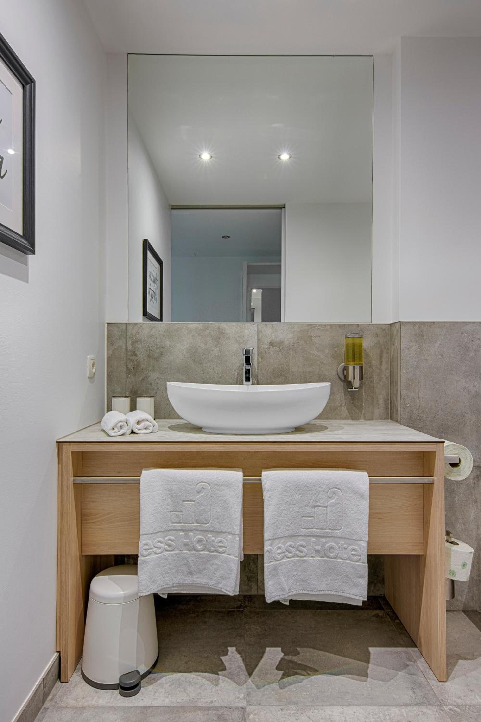 A modern bathroom with a large white sink, two towels, a toilet, and a mirror above the sink.