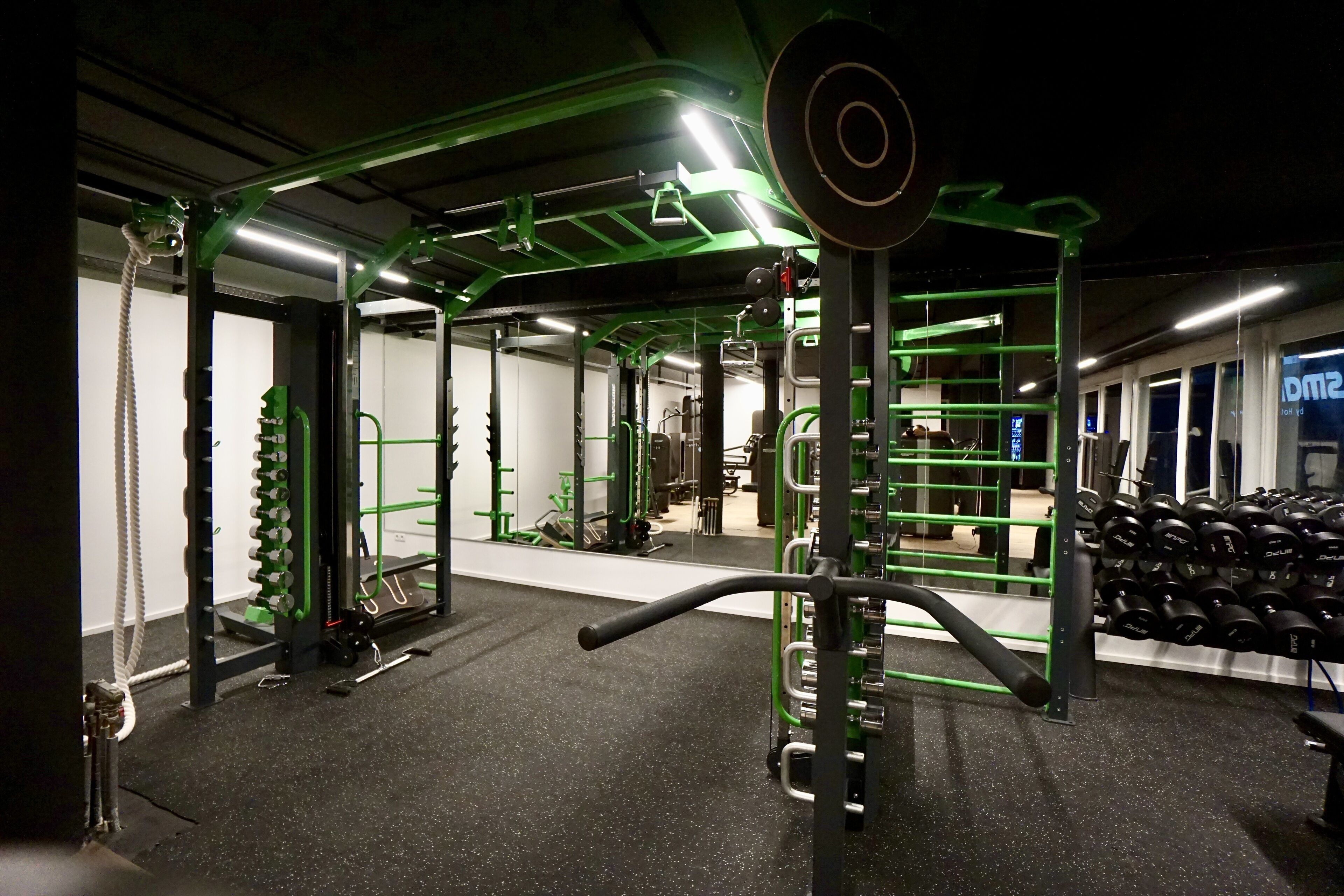 A gym with green equipment, weight racks, and a mirror.
