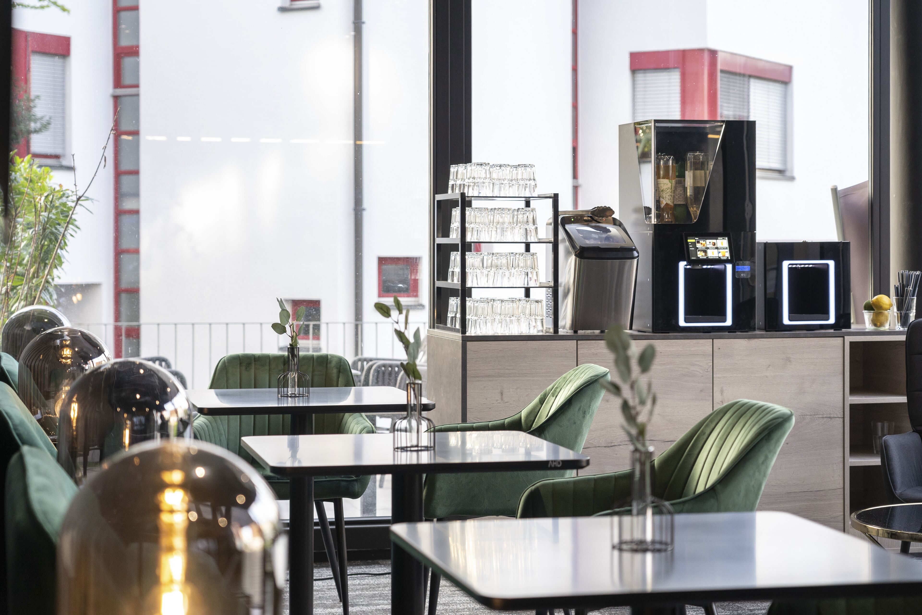 Een modern restaurant met groen stoffeerde stoelen, een glazen vitrine en een koffieapparaat.