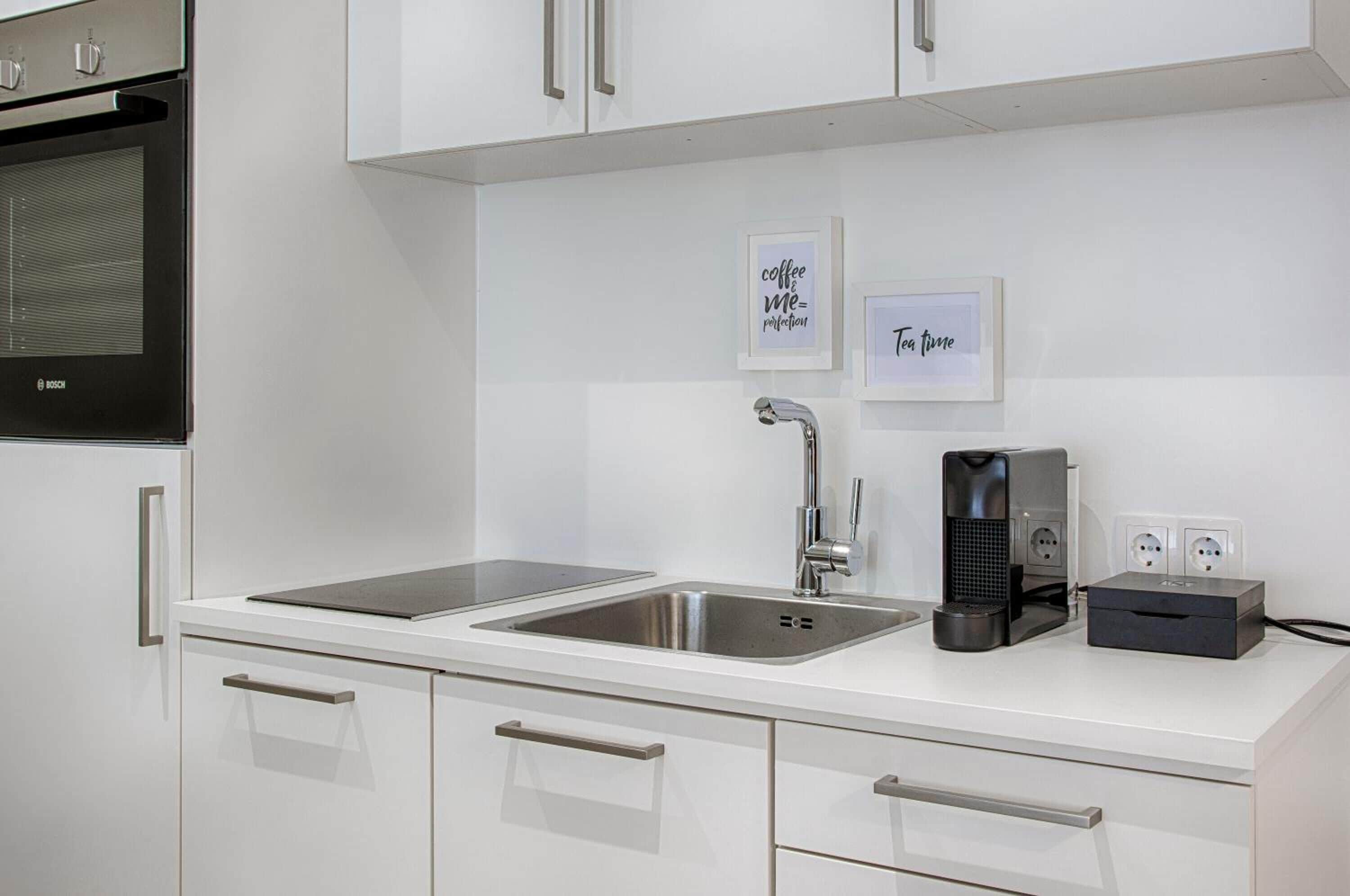 A modern kitchen with white cabinetry, a Bosch oven, a sink with a faucet, and two framed signs on the wall.