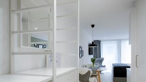 A modern, well-lit room with a white wardrobe, a dining area with a table and chairs, and a bed in the background.