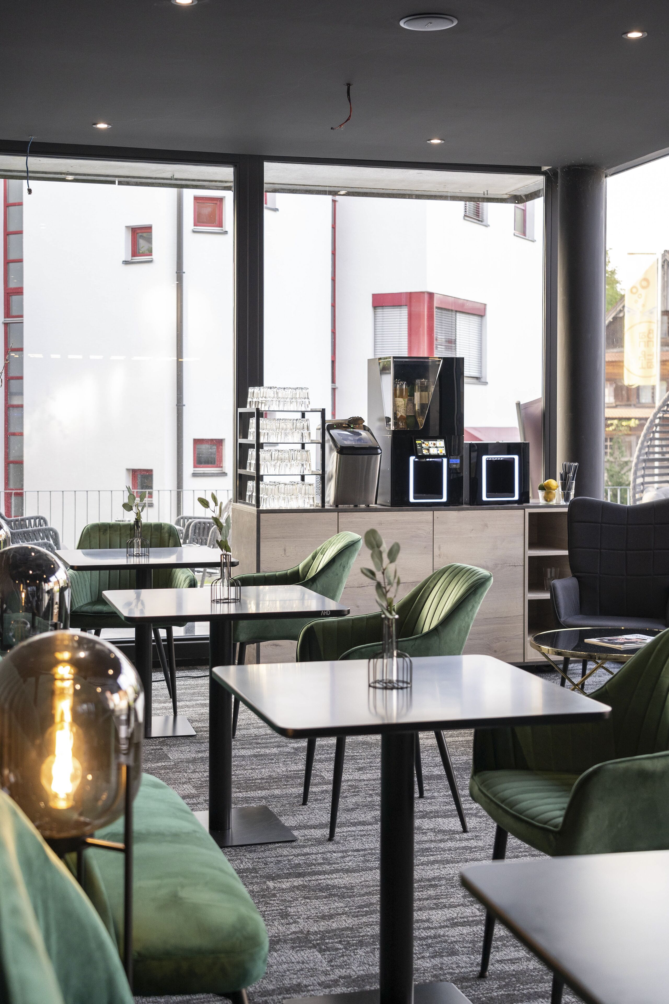 Een modern restaurantinterieur met groene beklede stoelen, tafels en een glazen displaykast.