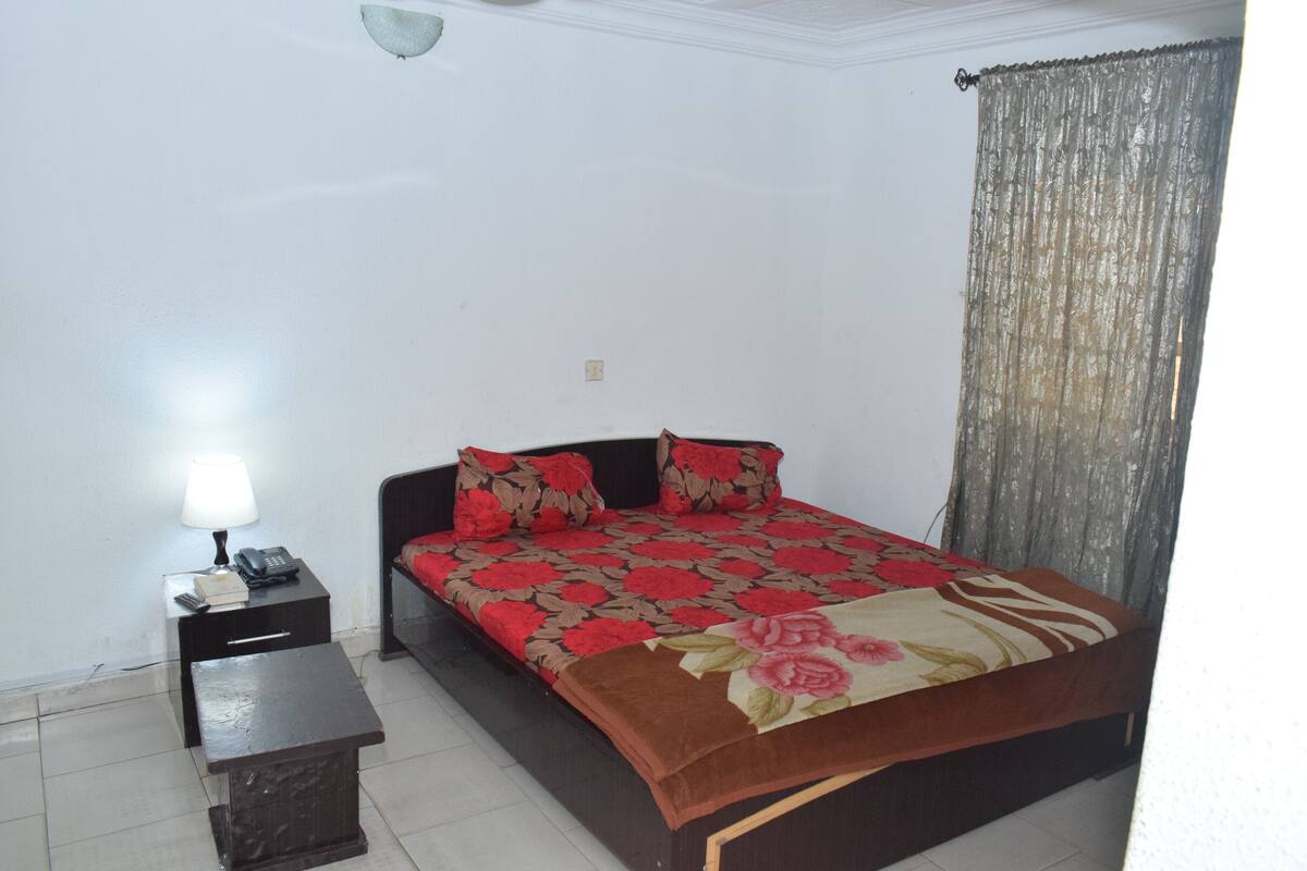 A bedroom with a bed, bedside table, lamp, and a small table.