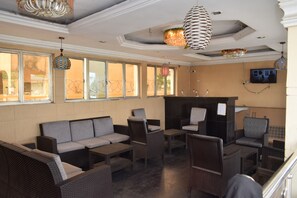 A lobby with wicker furniture, a fireplace, and large windows with a view of a barbed wire fence. - Wiltrice Hotel Limited (Ughelli)