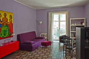 Ein Zimmer mit einem violetten Sofa, einem roten Schrank, einem Esstisch mit Stühlen und einem Fernseher.