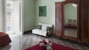 Une pièce avec un canapé blanc, une armoire en bois, un tapis rouge et un tableau vert accroché au mur.