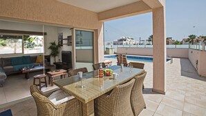 A spacious balcony with a glass table and wicker chairs, overlooking a swimming pool and a residential area.