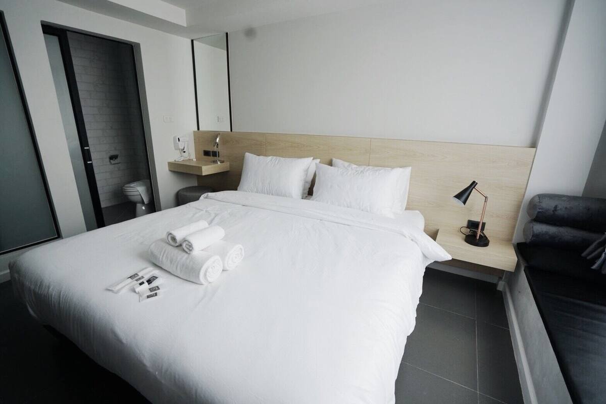 Ein modernes Hotelzimmer mit einem großen Bett, einem Nachttisch mit Lampe, einem Holz-Kopfteil und einem schwarzen Sessel.