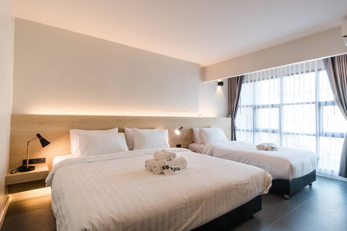 Ein Hotelzimmer mit zwei Betten, einem Nachttisch mit Lampe und einem großen Fenster mit Vorhängen.