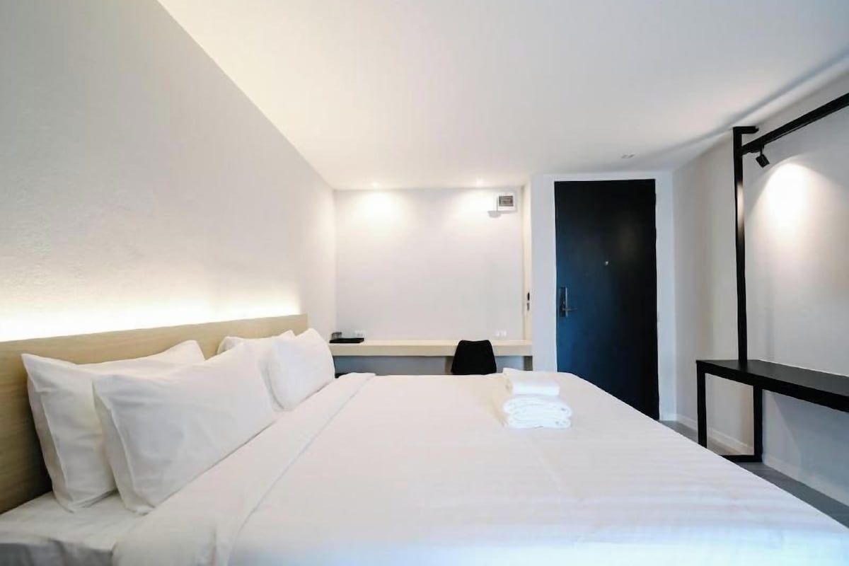 A hotel room with a large bed, a desk, and a door.
