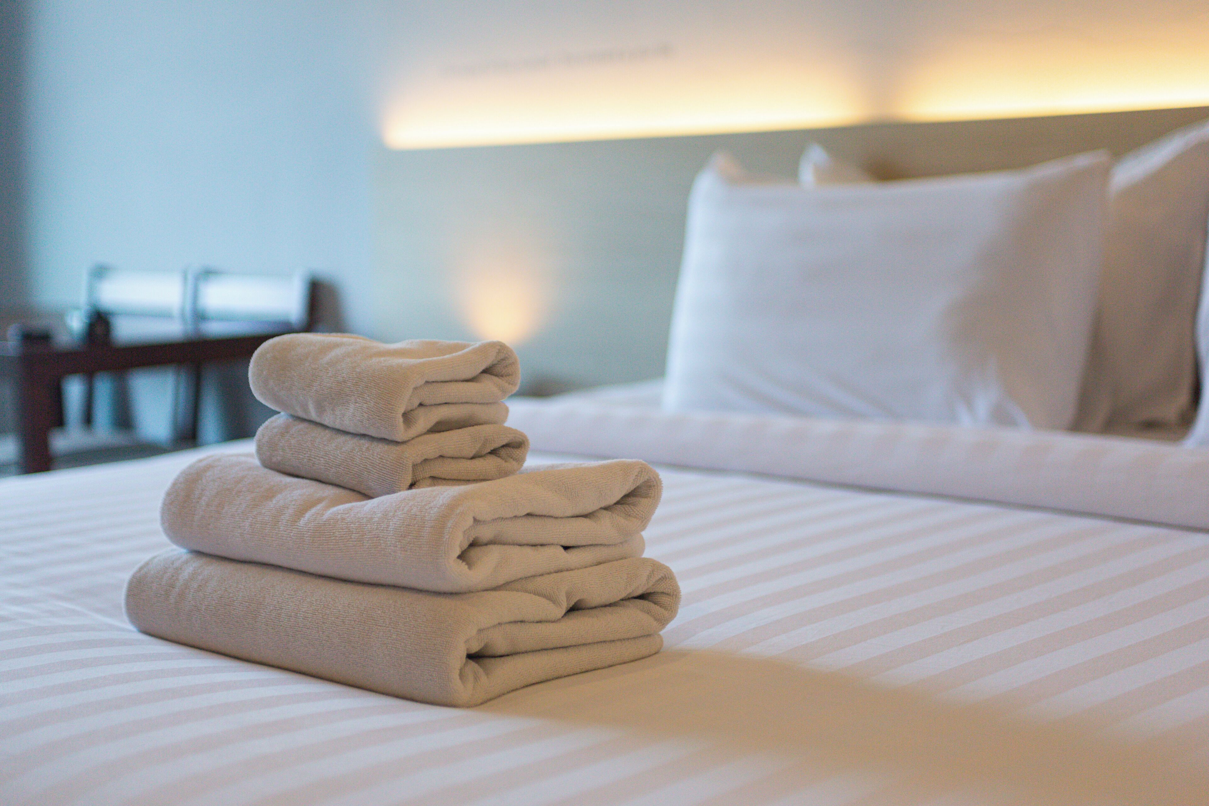 A neatly made bed with a stack of folded towels on the side.