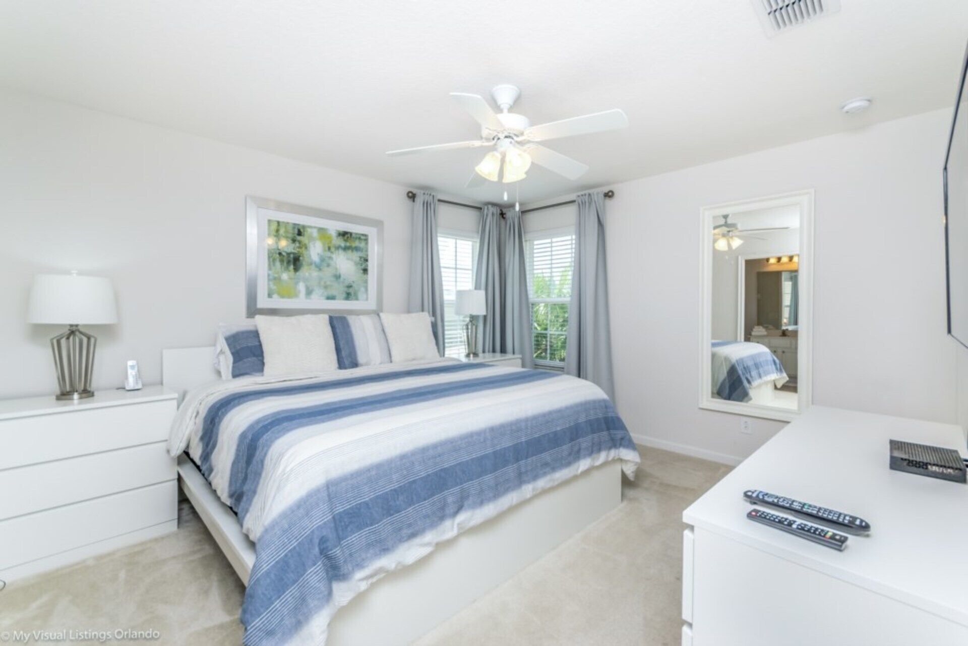 A bedroom with a bed, a nightstand, a desk, a ceiling fan, and a window with curtains.