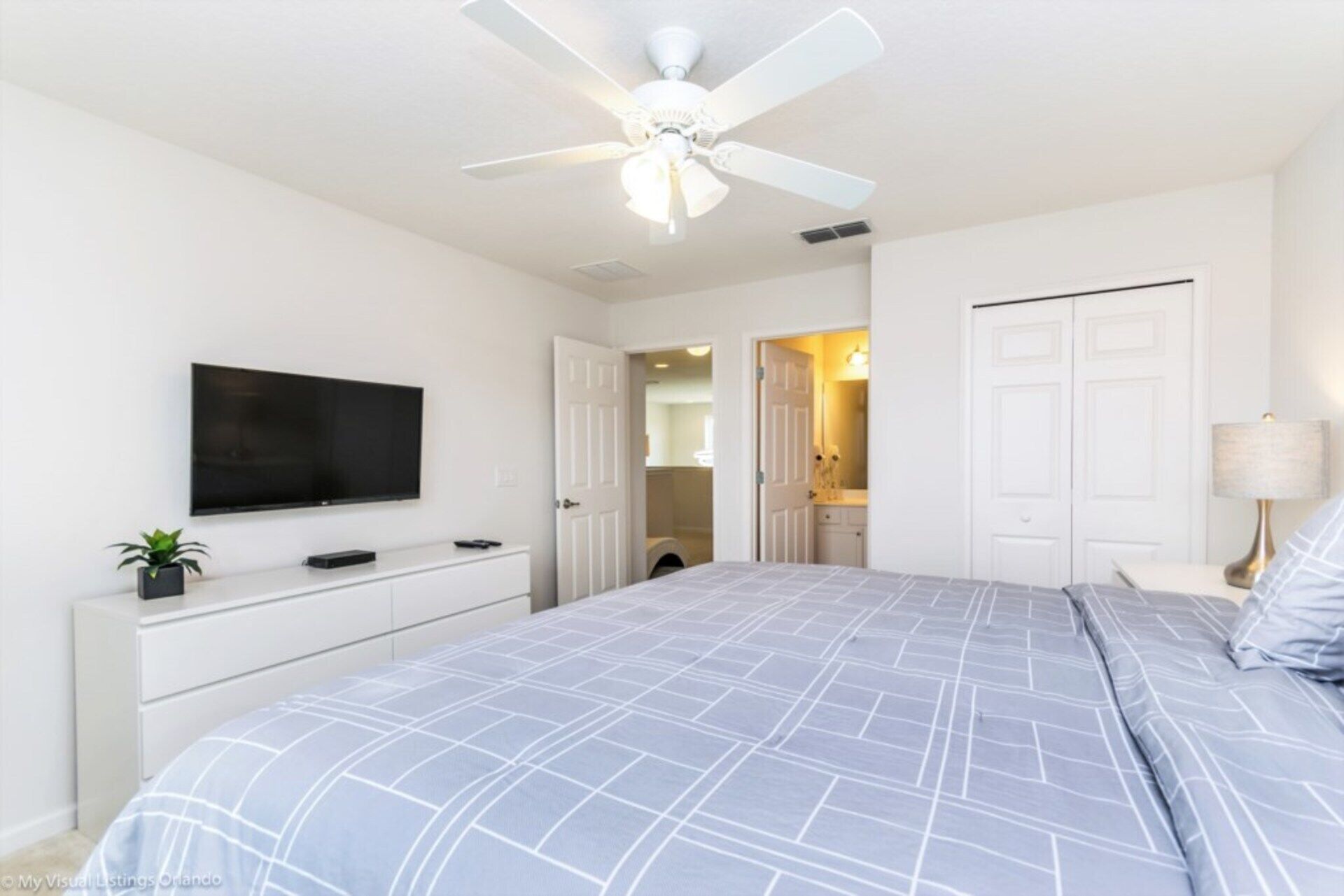 A bedroom with a bed, a ceiling fan, a TV, a dresser, and a door leading to a bathroom.