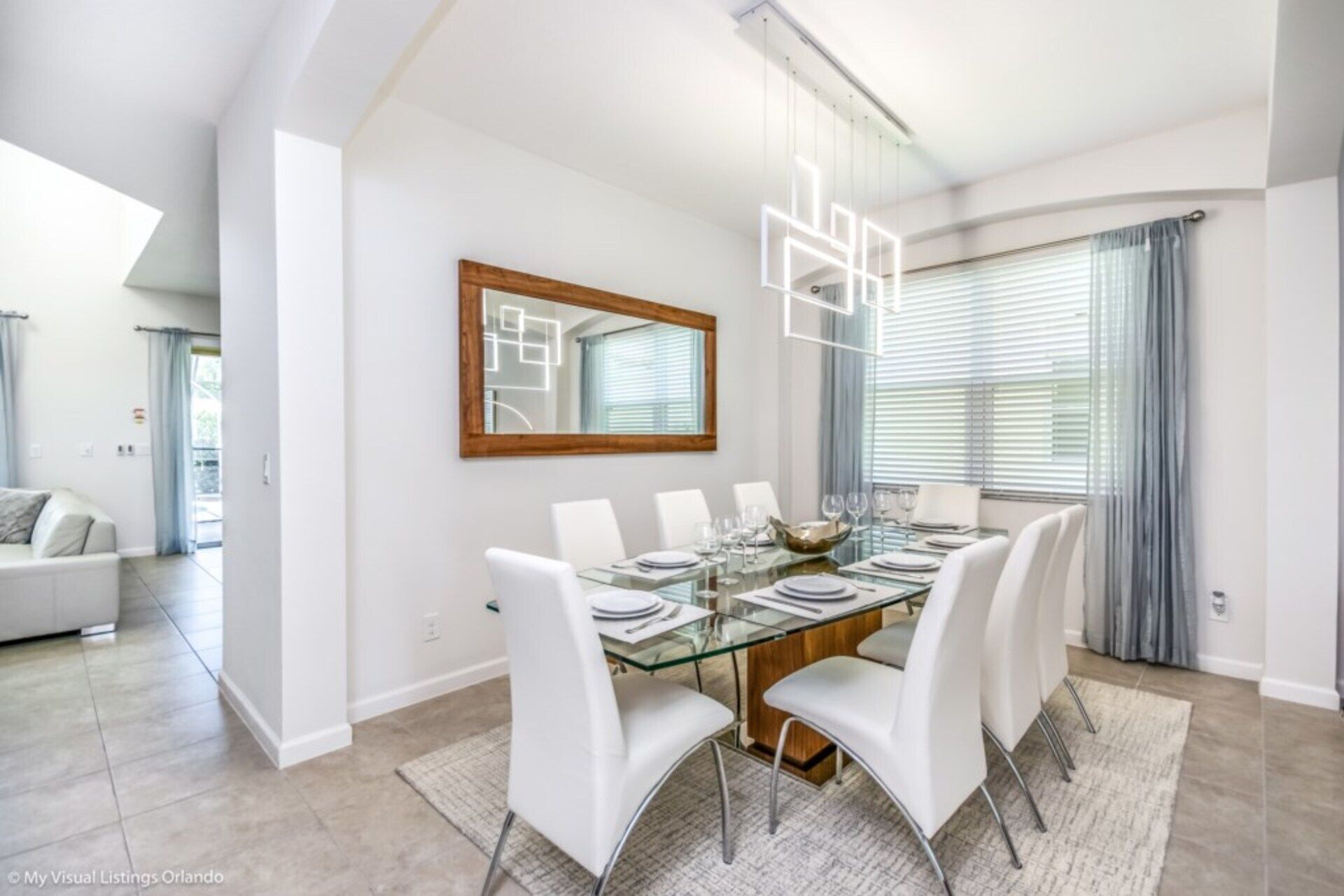 Uma sala de jantar com mesa de vidro, cadeiras brancas e um lustre moderno.