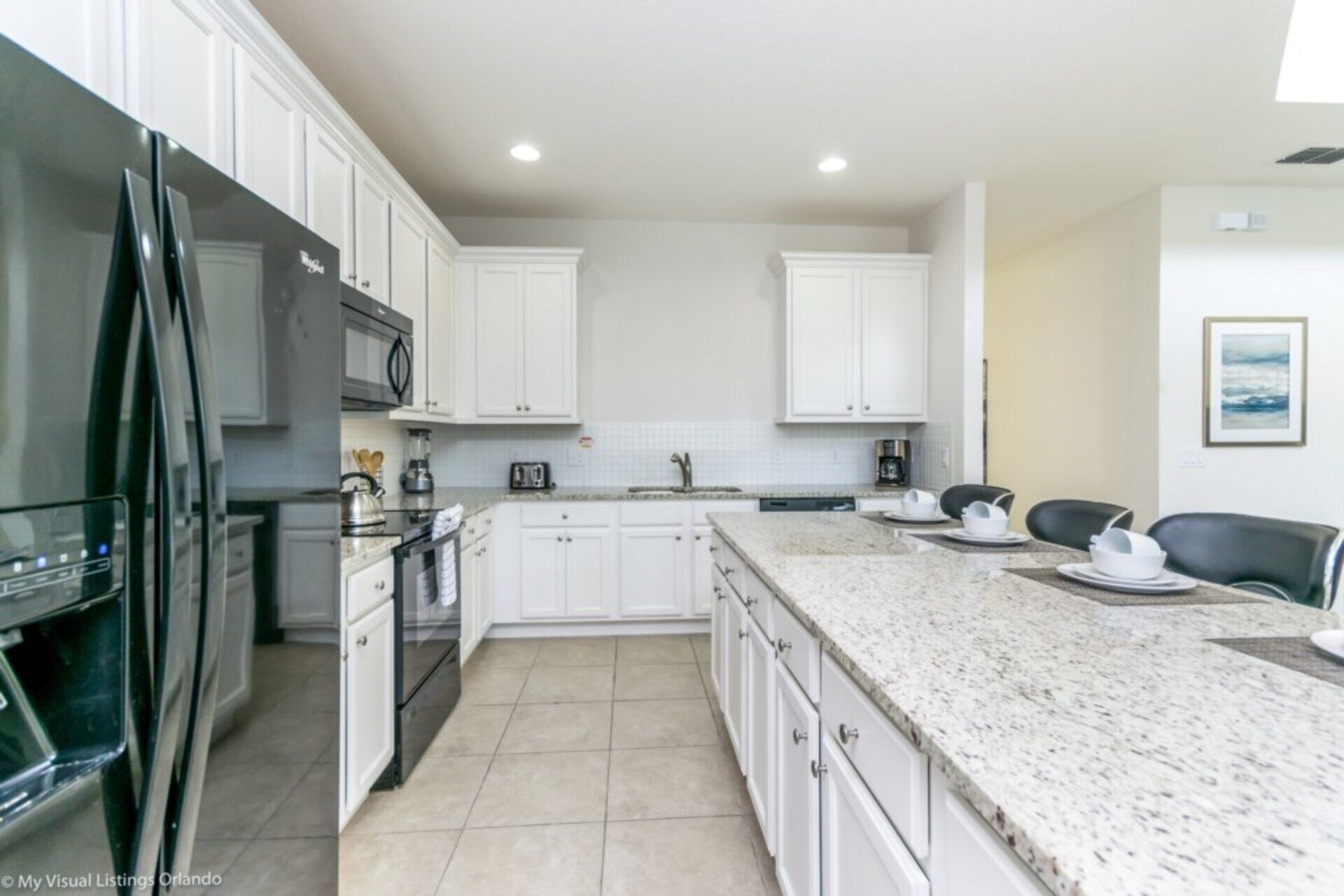 A modern kitchen with white cabinets, a granite countertop, and a stainless steel refrigerator.