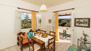 A dining area with a wooden table, chairs, and a hanging light fixture. - Artos Apartments (Rethymno)