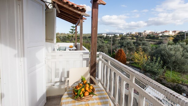 A balcony with a wicker basket of oranges, a white chair, and a view of a hilly landscape. - Artos Apartments (Rethymno)