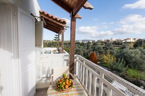 A balcony with a wicker basket of oranges, a white chair, and a view of a hilly landscape. - Artos Apartments (Rethymno)