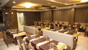A restaurant with multiple dining tables, each set with white plates, silverware, and brown napkins. - The Grand Vinayak Hotel (Ahmedabad)