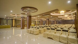 A spacious hall with rows of chairs covered in white fabric, a reception area with a yellow table, and a modern ceiling design with recessed lighting. - The Grand Vinayak Hotel (Ahmedabad)