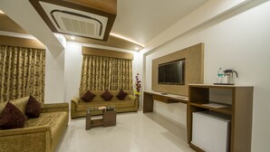 A modern living room with a sofa, coffee table, TV, and a small refrigerator. - The Grand Vinayak Hotel (Ahmedabad)