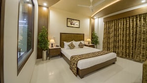 A modern hotel room with a large bed, two bedside tables with lamps, a ceiling fan, and a large window with curtains. - The Grand Vinayak Hotel (Ahmedabad)