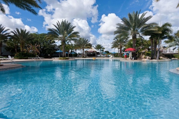 A large outdoor swimming pool surrounded by palm trees and a clear blue sky.