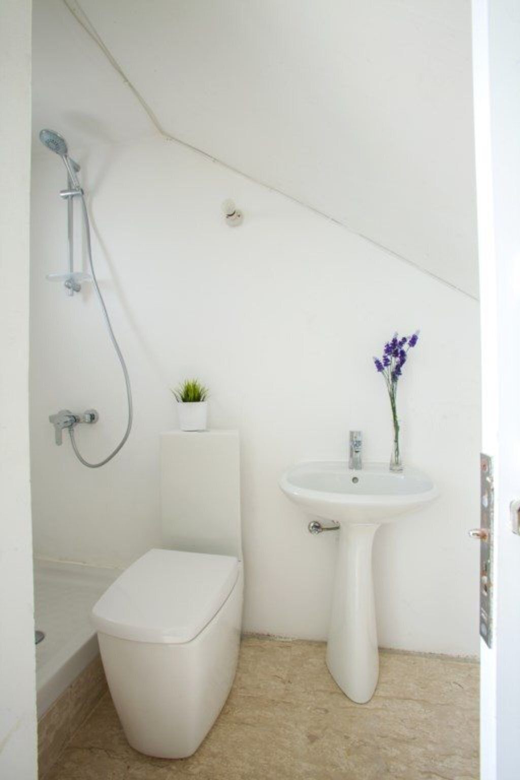 Un baño pequeño y blanco con un inodoro, un lavamanos pedestal y una ducha.
