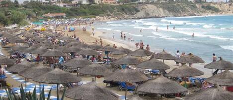 A beach with numerous thatched umbrellas and beach chairs, a sandy shore, and a view of the ocean.