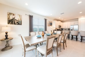 Une cuisine moderne avec des meubles blancs, un îlot central et un coin repas comprenant une table et des chaises en bois.