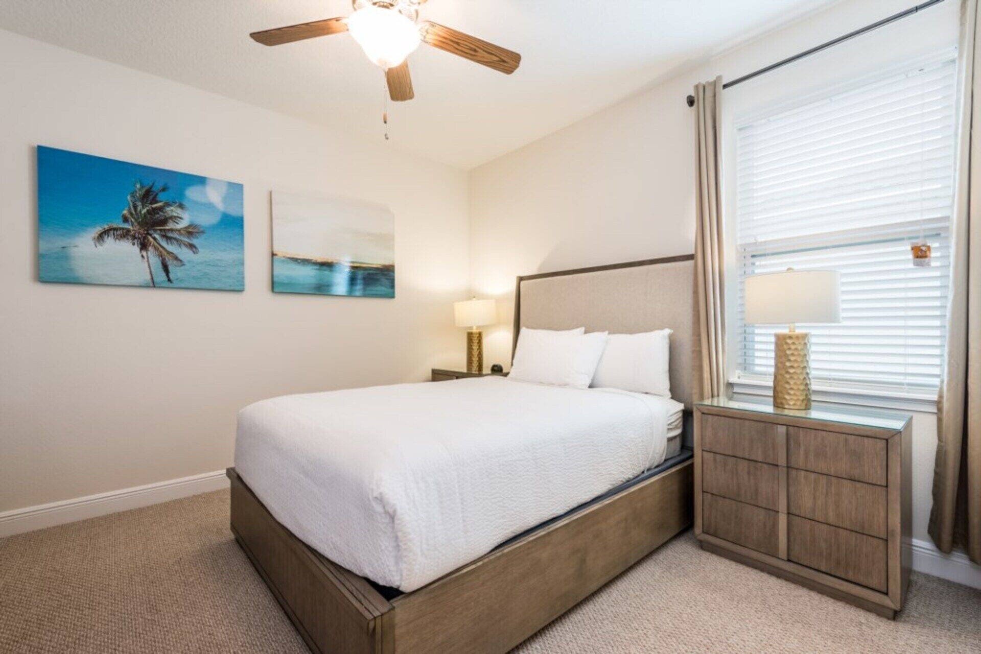 A neatly arranged bedroom with a bed, a ceiling fan, a nightstand with a lamp, and a window with blinds.