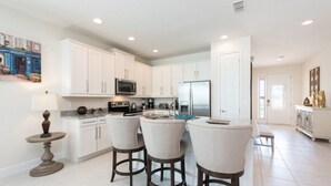 A modern kitchen with white cabinets, a stainless steel refrigerator, and a dining area with three bar stools.
