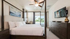 A four-poster bed with a ceiling fan, a television, and a view of the outdoors.