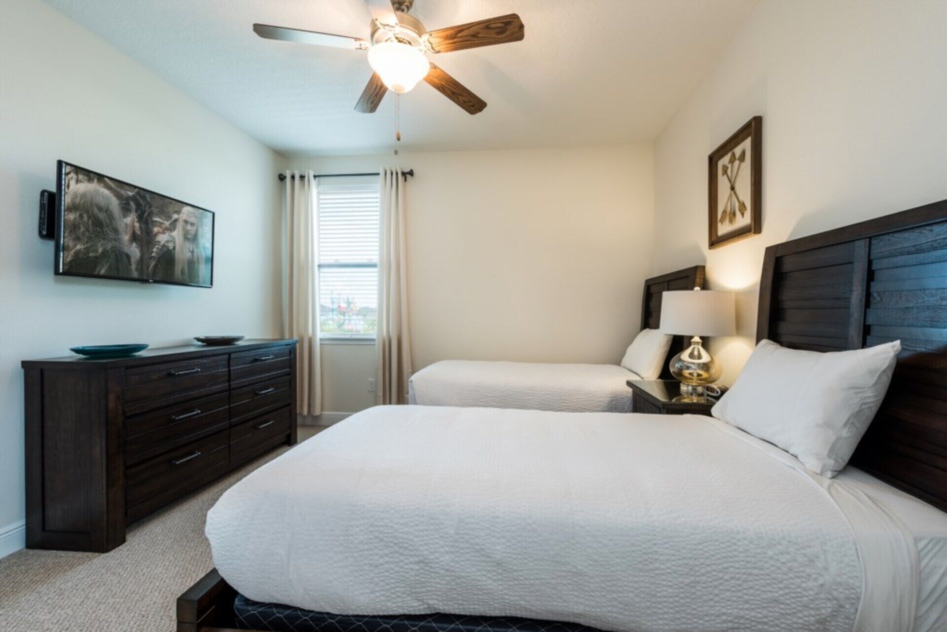 A bedroom with a large bed, a dresser, a ceiling fan, and a painting on the wall.