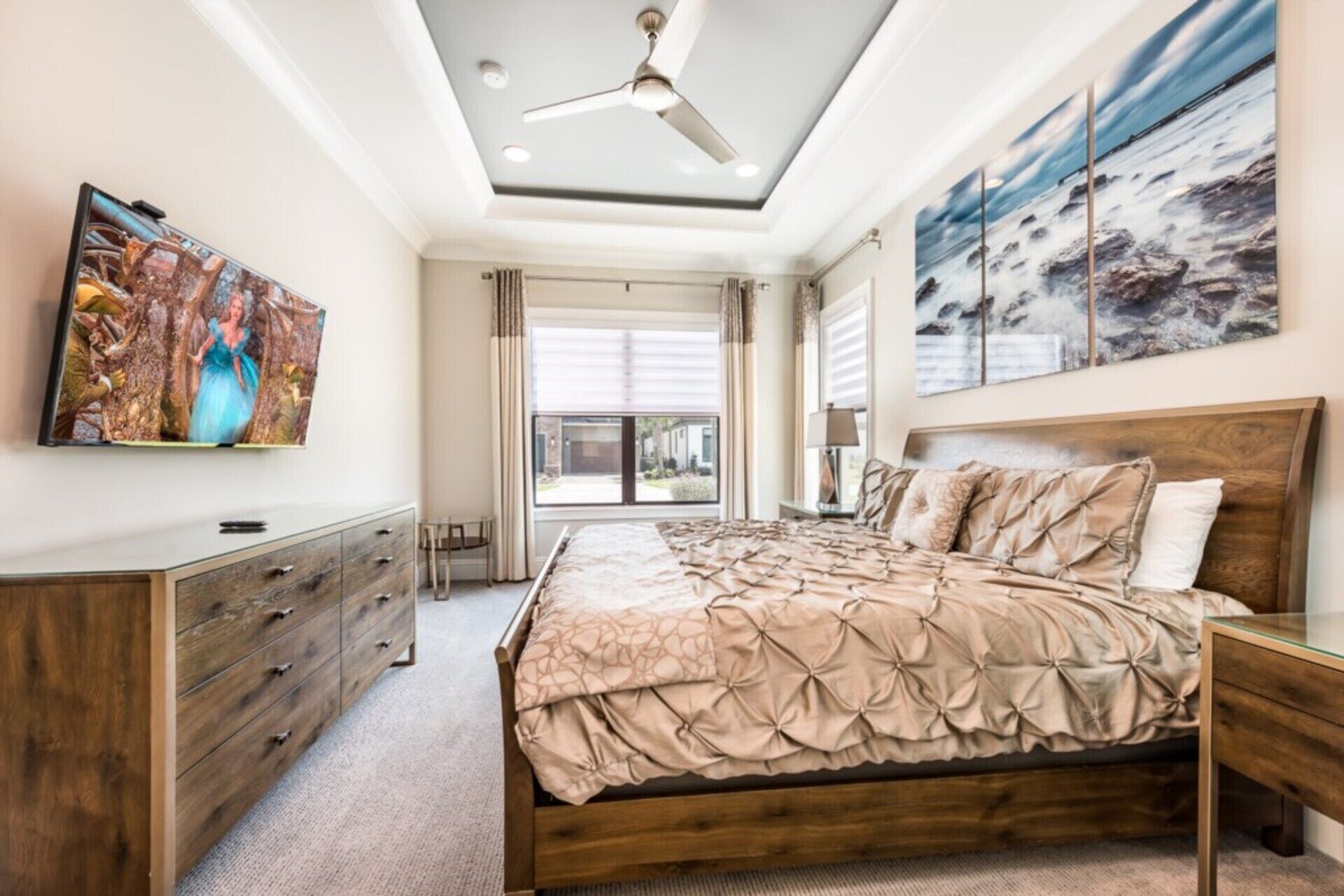 Une chambre à coucher avec un lit, une commode, un ventilateur de plafond et des œuvres d’art accrochées aux murs.