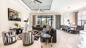 A modern living room with a sofa, coffee table, and TV. There is a dining area with chairs and a table. - Beautiful Villa With Private Pool, Close to Disney, Orlando Villa 2949 (Kissimmee)