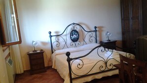 A bed with a metal frame and a decorative headboard, a bedside table with a lamp, and a chair. - Room in B&B - A Little Place in Tuscany Where to Relax (Montaione)