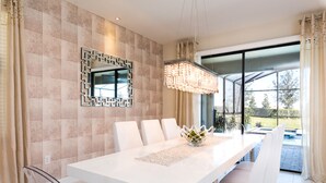 Un espace repas moderne avec une table blanche, des chaises transparentes et un miroir décoratif au mur.