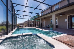 Piscina com estrutura de vidro, cercada por um terraço com assentos e plantas em vasos.